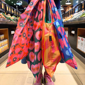 Colorful reusable shopping bags with fruit patterns in a grocery store.